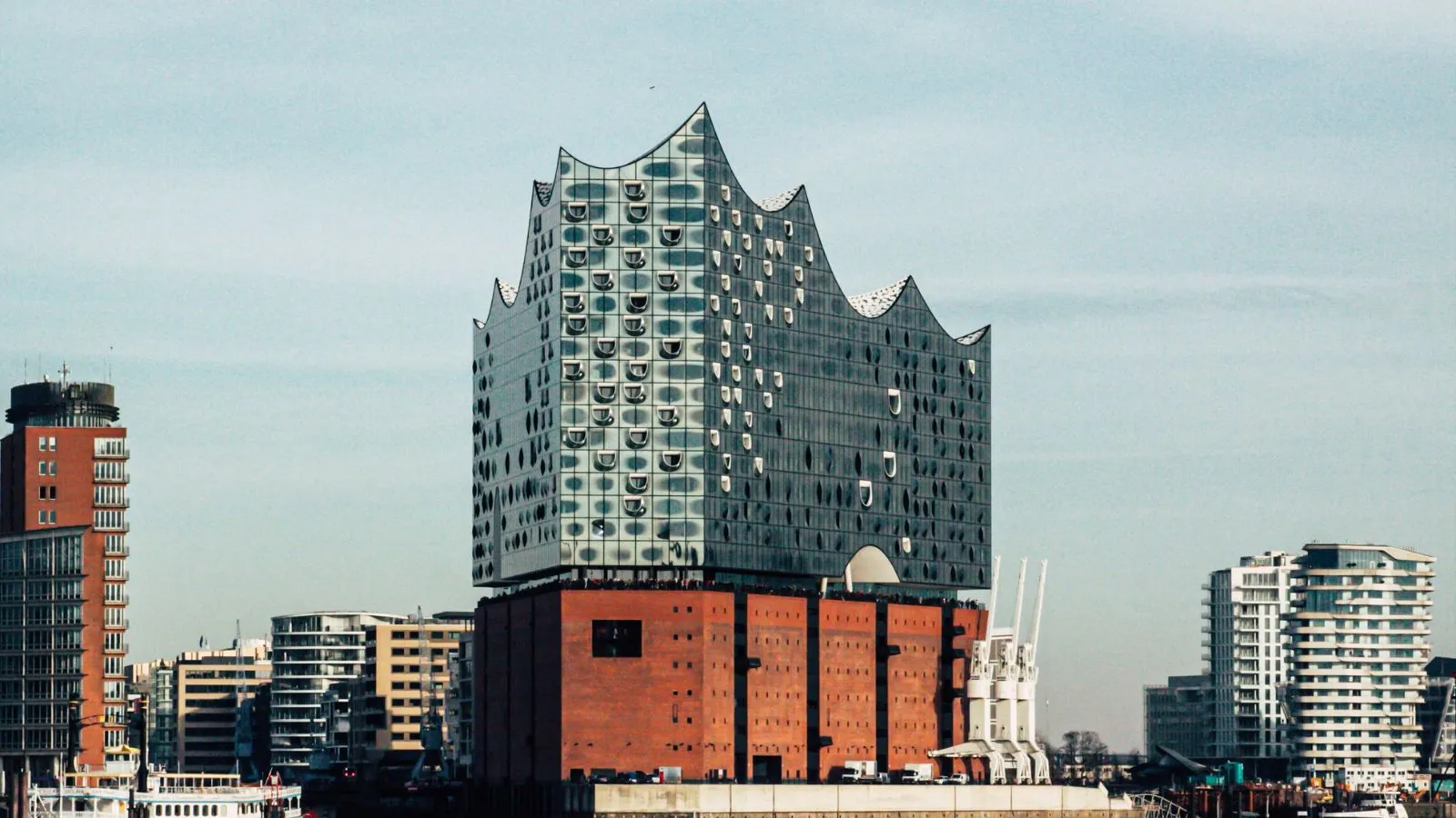 Das Bild zeigt die Elbphilharmonie Konzerthalle mit ihrer wellenförmigen Glasfassade, die sich in Hamburg, Deutschland, gegen einen klaren Himmel abzeichnet.